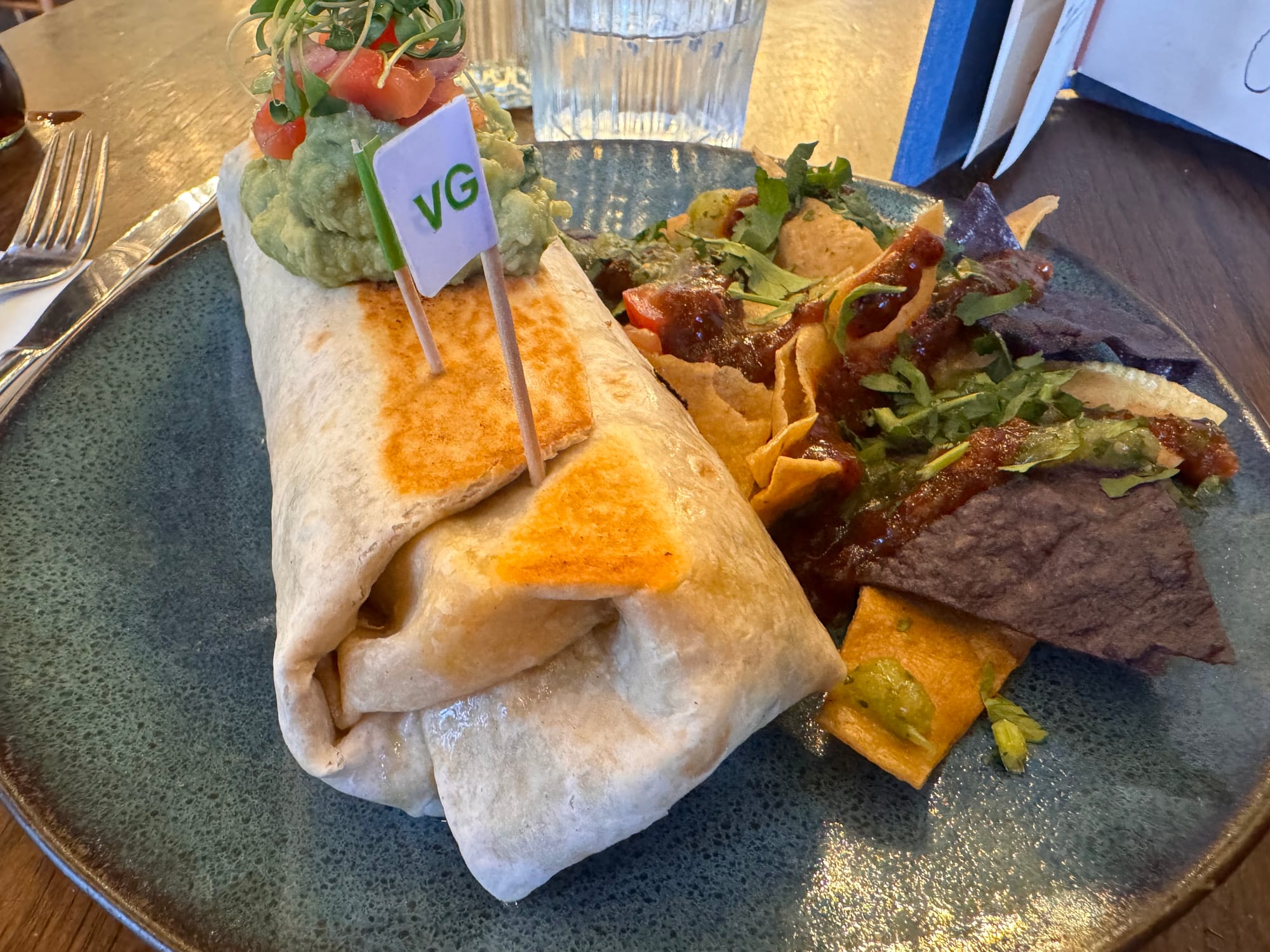 A burrito—with a big pile of guacamole on top of it—next to some tortilla chips on a plate.