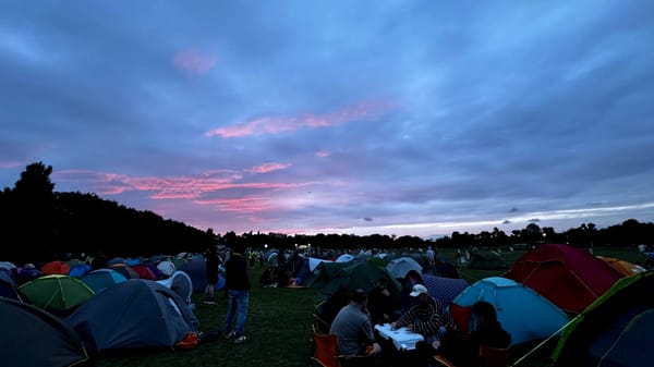 A large group of tents and people, with a lovely red sunset in the background.