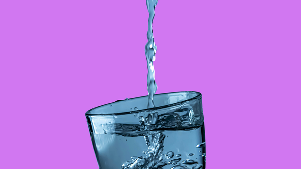 Water being poured into a glass on a solid purple background.